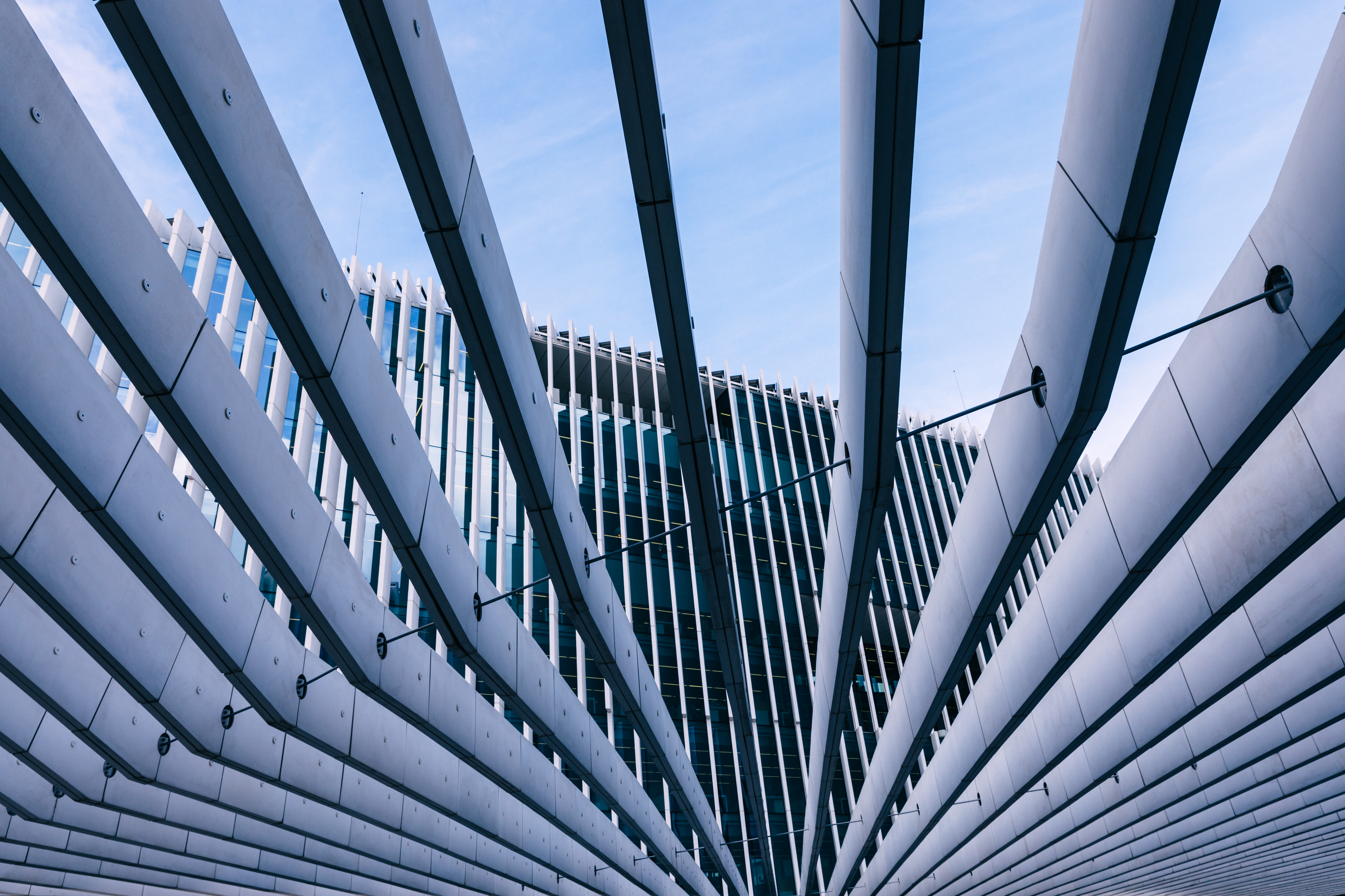 Upward view of glass and steel beams intersecting against the sky, forming a dynamic architectural composition